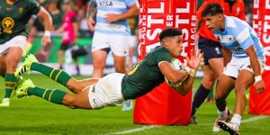 South African rugby player Sacha Feinberg-Mngomezulu in a green and gold Springbok jersey diving horizontally through the air to score a try against Argentina.