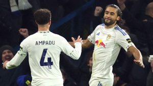 Dominic Calvert-Lewin, wearing a white Leeds United home kit with a Red Bull logo, smiles and celebrates a goal at Elland Road. He is facing teammate Ethan Ampadu, who has his back to the camera showing the name "AMPADU" and the number 4 on his shirt.
