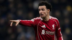 Liverpool midfielder Curtis Jones, featuring his signature curly hair and beard, wearing the red 2025/26 home kit and pointing toward the field to direct his teammates during a Premier League match.