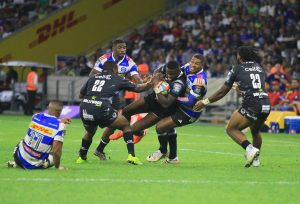 A high-intensity rugby match featuring players from the DHL Stormers in blue and white striped jerseys and the Sharks in black jerseys with "cell C" and "Hollywood bets" branding.